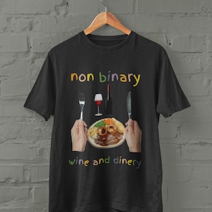 May include: Black t-shirt with the text "non binary wine and dinery" in rainbow colors. The design includes a fork, knife, glass of wine, bottle of wine, and a plate of food.
