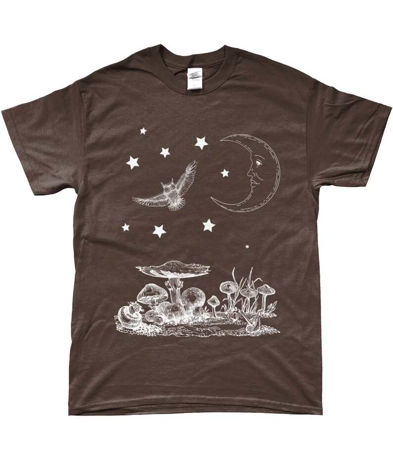 May include: A brown t-shirt with a white graphic design of an owl flying under a crescent moon with a face. There are stars and mushrooms in the design.