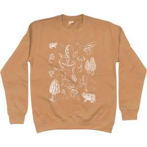 May include: A tan long-sleeve sweatshirt with a white graphic print of frogs and mushrooms.