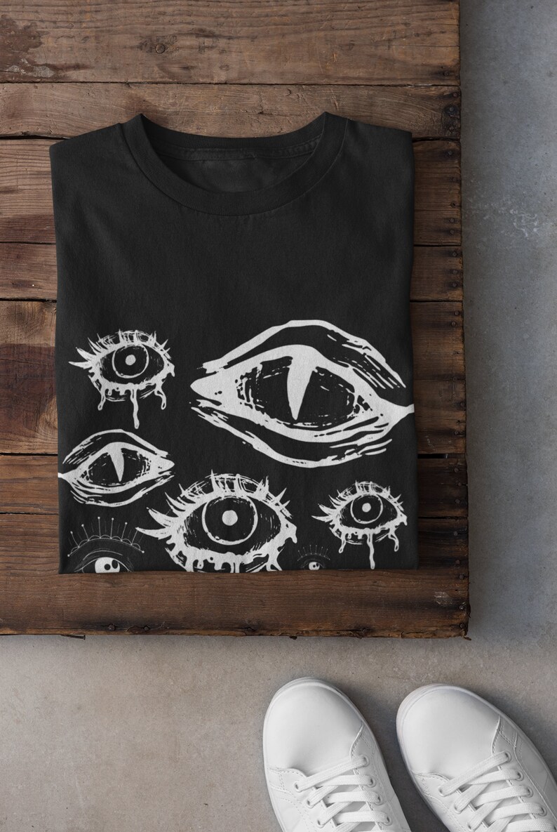 May include: Black t-shirt with a white print of multiple stylized eyes. The eyes are drawn in a graphic style with dripping lines.