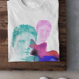 May include: White t-shirt with a graphic design featuring two faces of classical sculptures in shades of teal and pink, with a colorful abstract shape behind them.