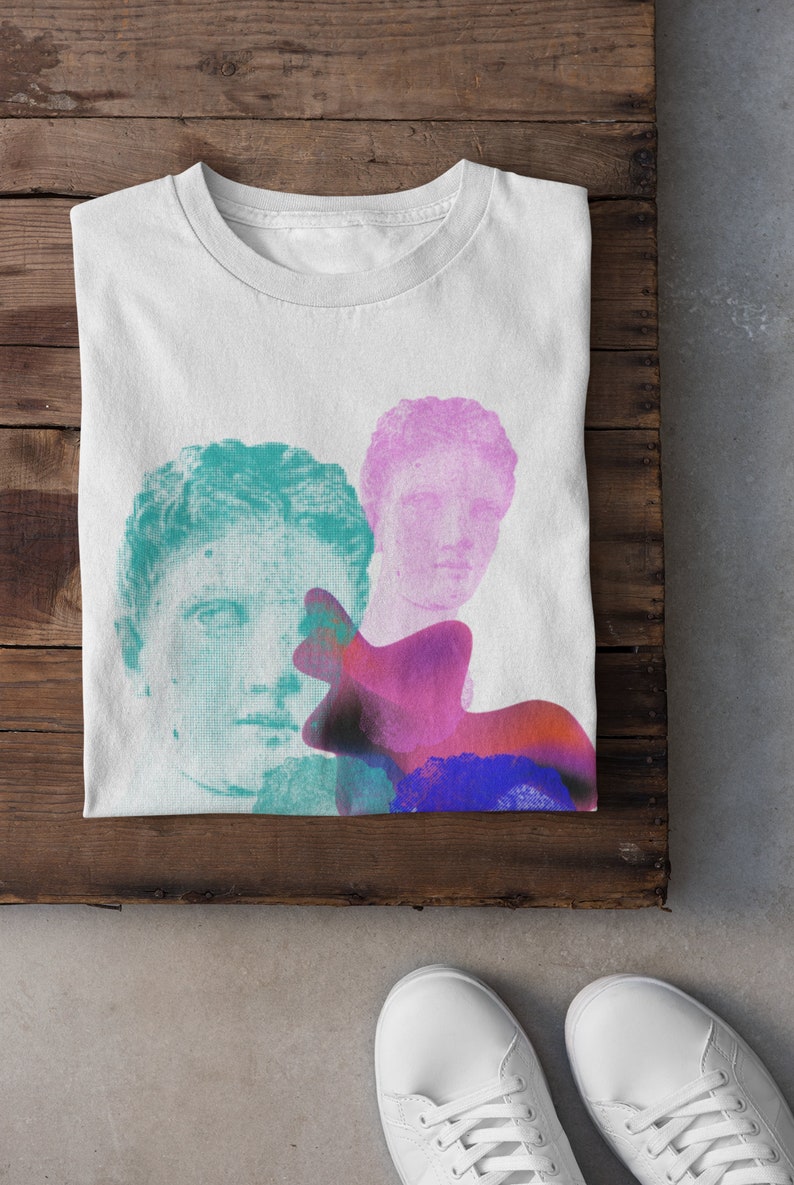 May include: White t-shirt with a graphic design featuring two faces of classical sculptures in shades of teal and pink, with a colorful abstract shape behind them.