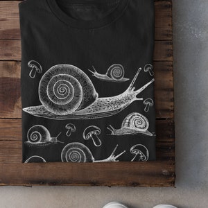 May include: Black t-shirt with a white graphic print of snails and mushrooms. The snails are drawn in a vintage style.
