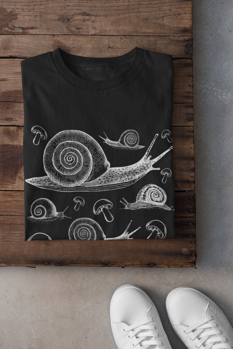 May include: Black t-shirt with a white graphic print of snails and mushrooms. The snails are drawn in a vintage style.