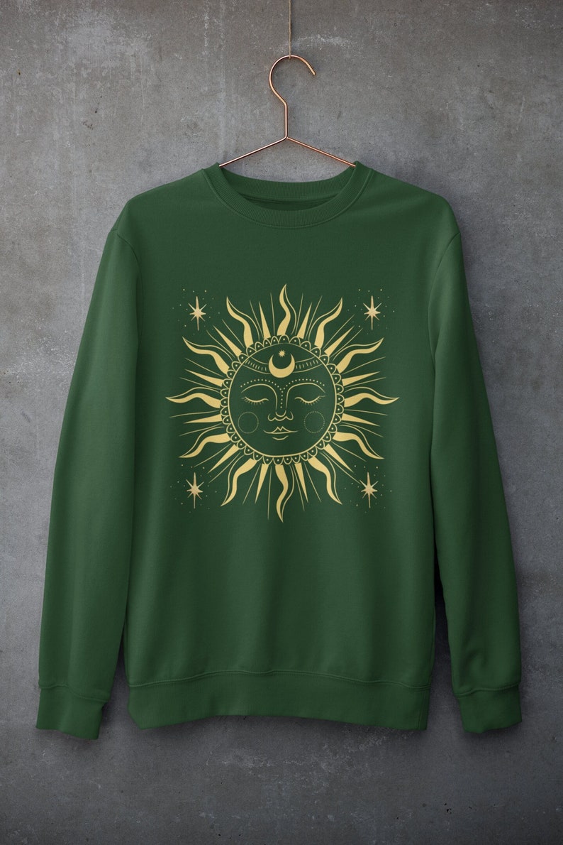 May include: A dark green sweatshirt with a gold sun and moon design. The sun has a face and is surrounded by stars.