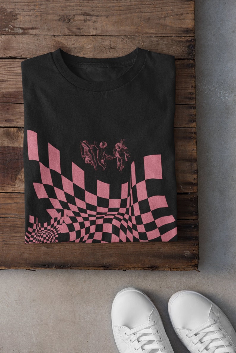 May include: Black t-shirt featuring a pink and black checkered pattern with three figures in the centre. The checkered pattern is distorted to create a wavy effect.