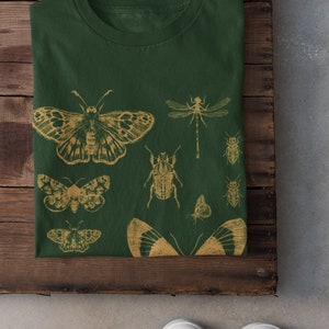 May include: A dark green t-shirt with a gold insect print. The print features butterflies, beetles, and dragonflies.