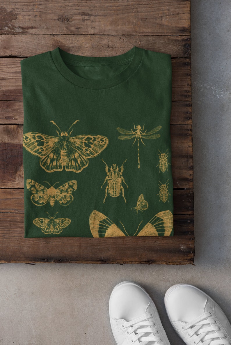May include: A dark green t-shirt with a gold insect print. The print features butterflies, beetles, and dragonflies.