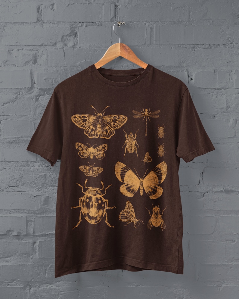 May include: A brown t-shirt with a vintage-style print of various insects and butterflies in gold. The insects include a dragonfly, beetles, and moths.