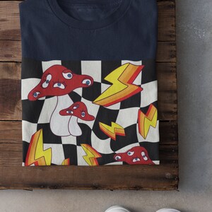 May include: A navy blue t-shirt with a checkered pattern featuring red mushrooms with eyes and yellow lightning bolts.