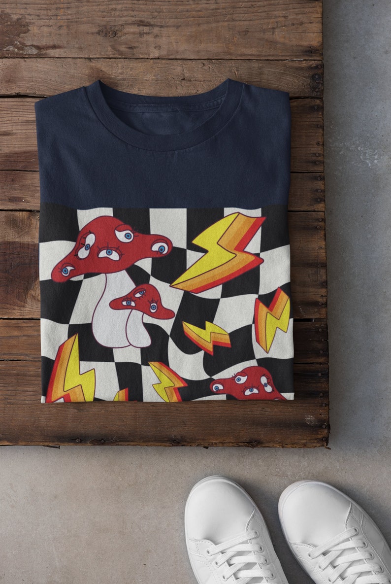 May include: A navy blue t-shirt with a checkered pattern featuring red mushrooms with eyes and yellow lightning bolts.