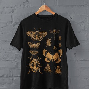 May include: Black t-shirt with a gold print of various insects and butterflies, including a dragonfly, a beetle, and a moth.