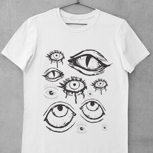 May include: White t-shirt with a black and white graphic print of multiple eyes. The eyes are drawn in a stylized, abstract style.