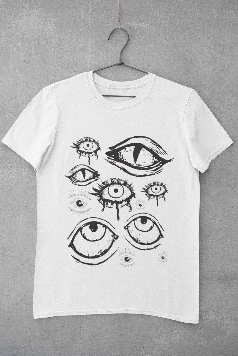 May include: White t-shirt with a black and white graphic print of multiple eyes. The eyes are drawn in a stylized, abstract style.