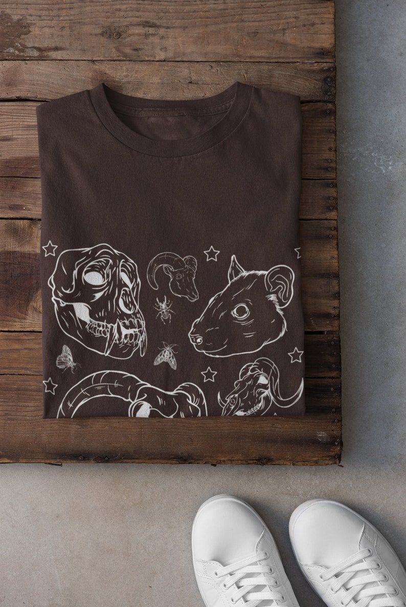 May include: A brown t-shirt with a white graphic print of animal skulls, insects, and stars.