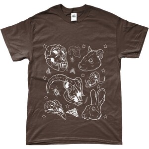 May include: A brown t-shirt with a white design of various animal skulls, insects, and stars. The design includes a monkey skull, a ram skull, a rat skull, a rabbit skull, a bird skull, and a rabbit.