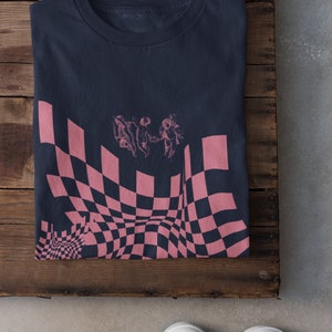 May include: A dark blue t-shirt featuring a pink and black checkered pattern with three cherubs in the centre.