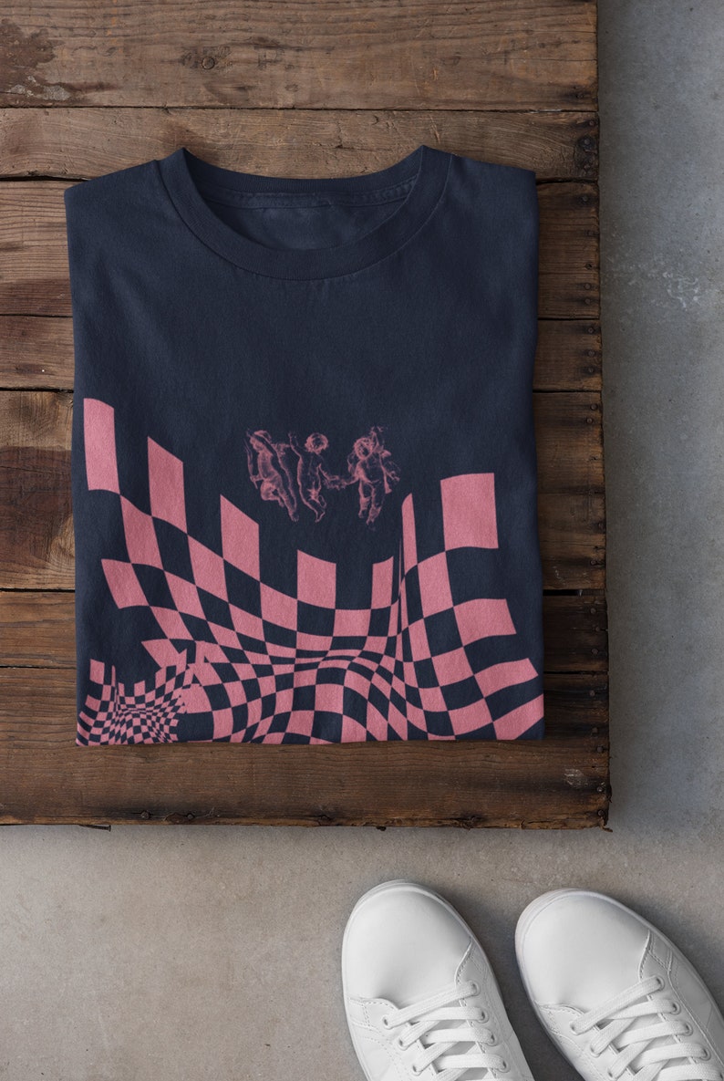 May include: A dark blue t-shirt featuring a pink and black checkered pattern with three cherubs in the centre.