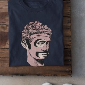 Puede incluir: Una camiseta azul marino con un gr&aacute;fico de un busto rosa de un hombre con bigote y barba negros.