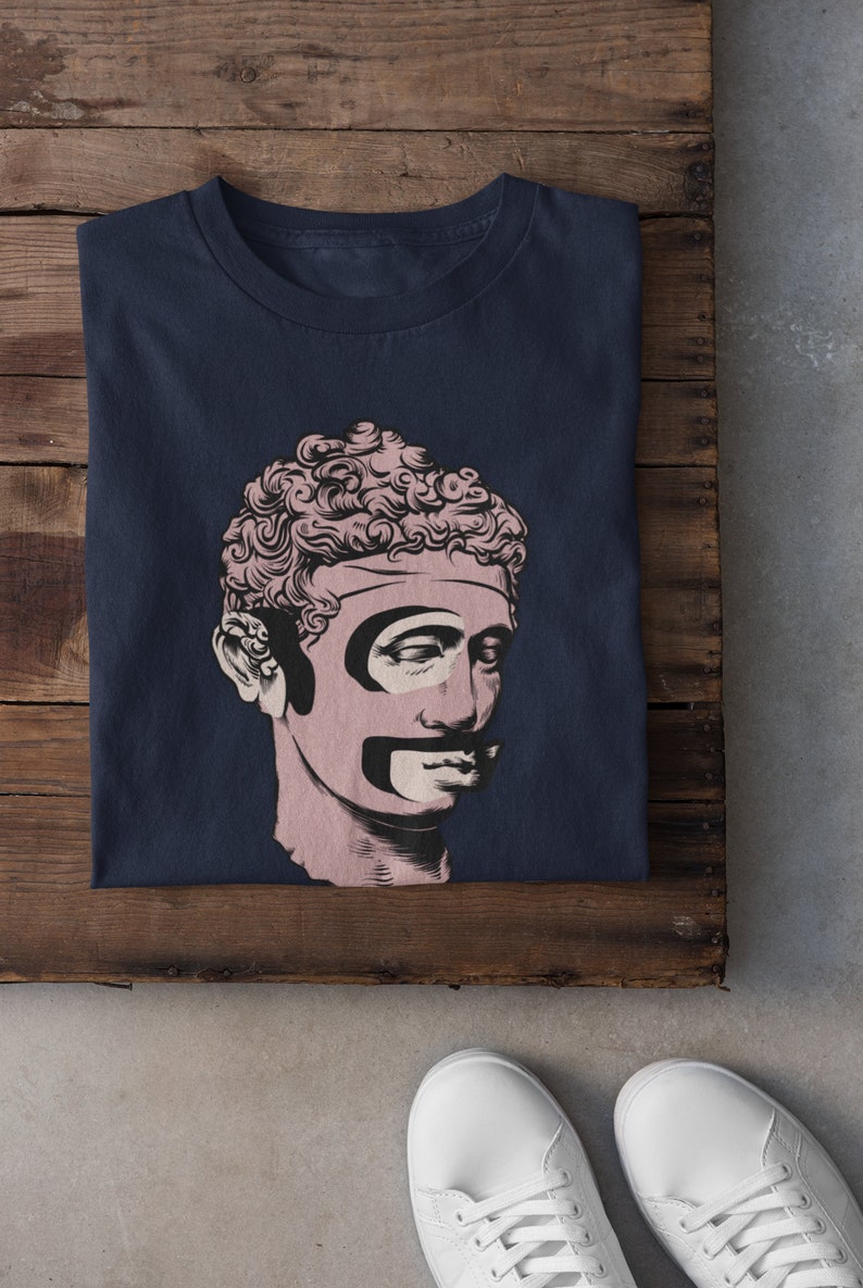 Puede incluir: Una camiseta azul marino con un gr&aacute;fico de un busto rosa de un hombre con bigote y barba negros.