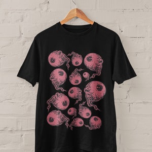 May include: Black t-shirt with a graphic print of pink eyes with black pupils. The eyes are surrounded by a swirling pattern.