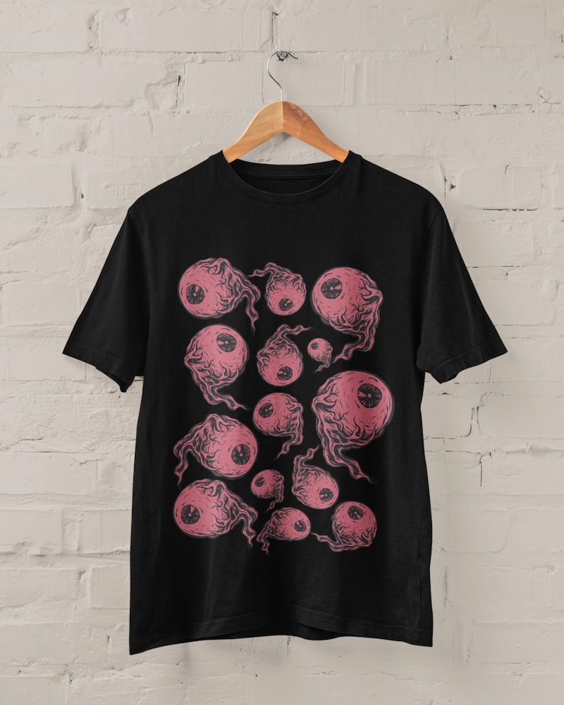 May include: Black t-shirt with a graphic print of pink eyes with black pupils. The eyes are surrounded by a swirling pattern.