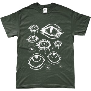 May include: Dark green t-shirt featuring a white graphic of multiple stylized eyes. The eyes vary in size and design, some with teardrop details. The shirt is a solid color, with a crew neck and short sleeves.