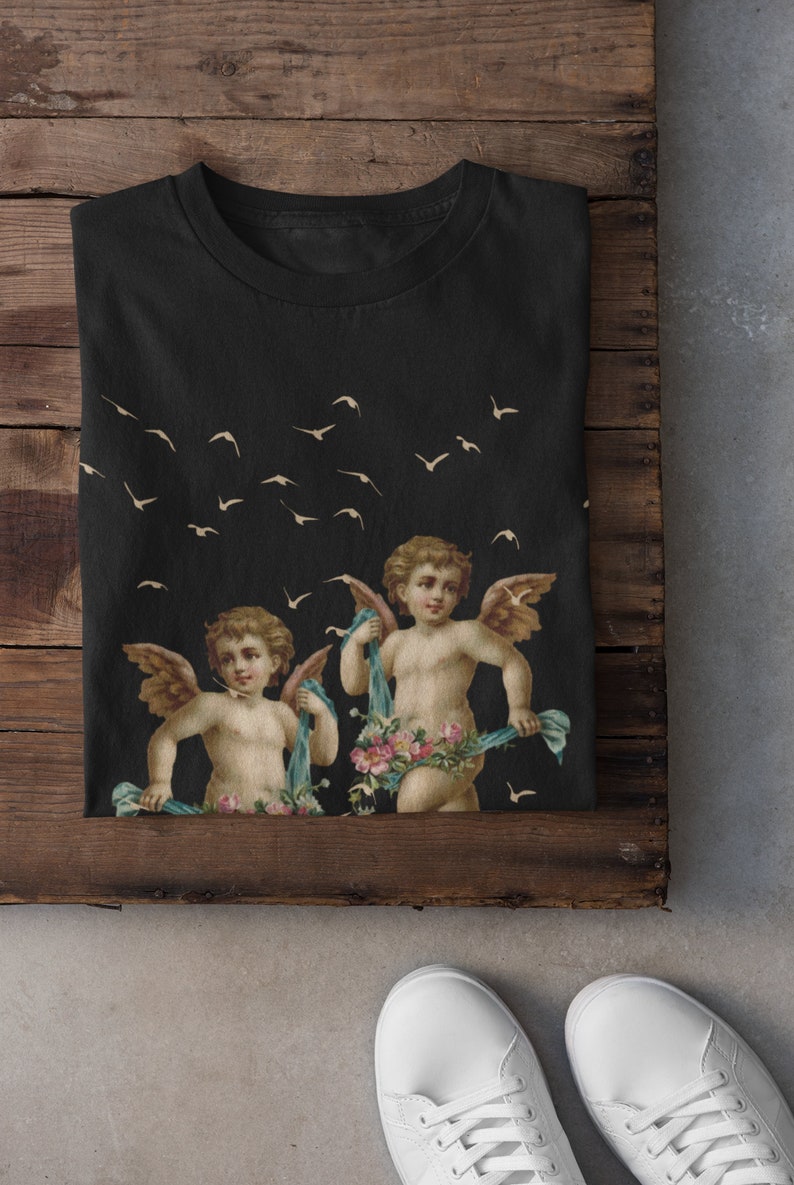 May include: Black t-shirt with a graphic print of two cherubs with wings and floral garlands, flying against a background of white birds.