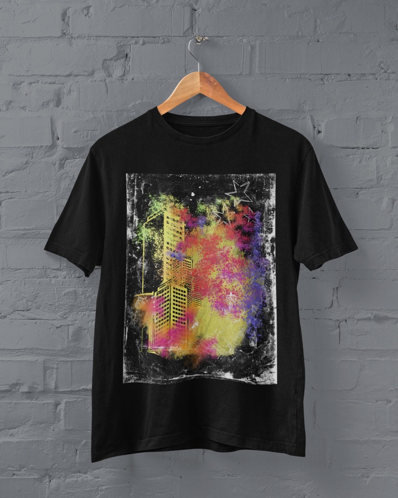 K&ouml;nnte beinhalten: Schwarzes T-Shirt mit einem grafischen Druck eines Stadtbildes in Gelb, Rosa und Blau mit einem Grunge-Effekt. Die Grafik ist von einem wei&szlig;en Rand umgeben.