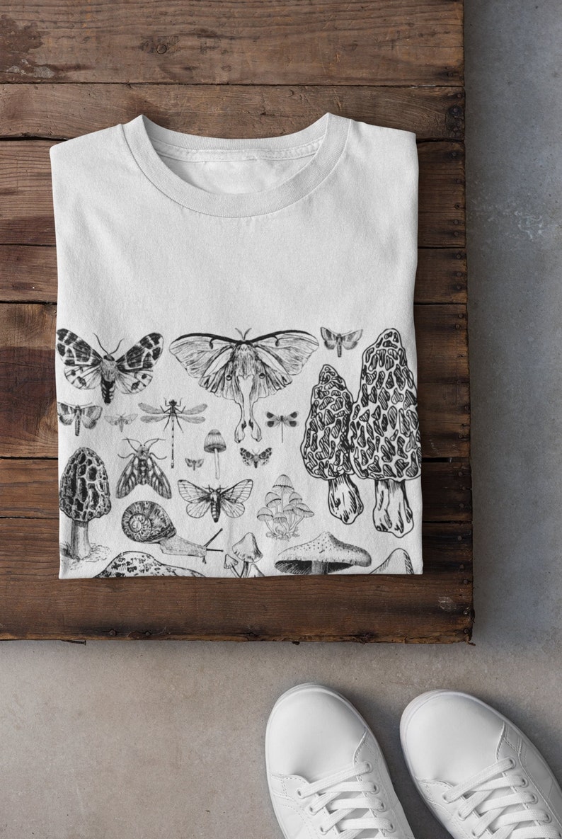 Puede incluir: Camiseta blanca con una ilustraci&oacute;n en blanco y negro de setas, mariposas y otros insectos.