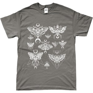 May include: A charcoal grey t-shirt with a white graphic print of moths and geometric shapes. The moths are stylized and have intricate details. The geometric shapes are triangles and crescents.