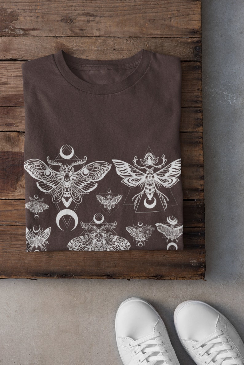 May include: A brown t-shirt with a white print of moths and crescent moons. The print is a repeating pattern of moths and moons.