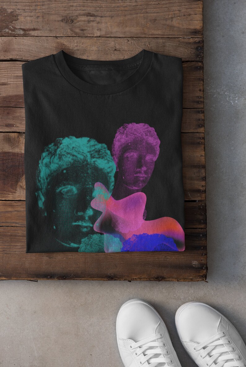 May include: Black t-shirt with a graphic print of three faces in shades of green, pink, and blue. The faces are stylized and appear to be from ancient sculptures.