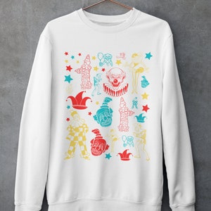 May include: White sweatshirt with a colorful print of various clowns, stars, and jester hats.