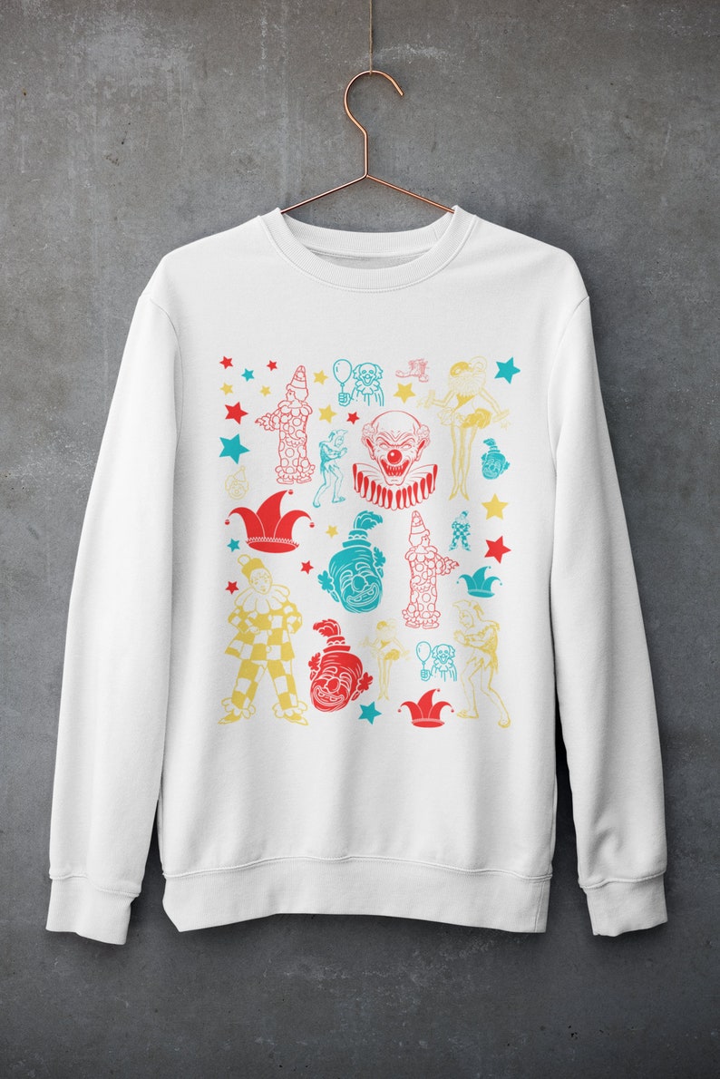 May include: White sweatshirt with a colorful print of various clowns, stars, and jester hats.