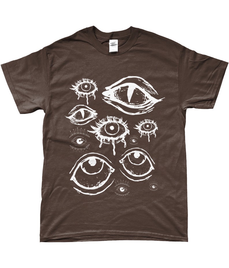 May include: A brown t-shirt with a white graphic print of multiple stylized eyes. The eyes are drawn in a variety of shapes and sizes, some with eyelashes and some with tears.