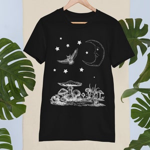 May include: Black t-shirt with a white graphic design of a crescent moon, an owl flying, and mushrooms. The design is reminiscent of a night sky with stars.