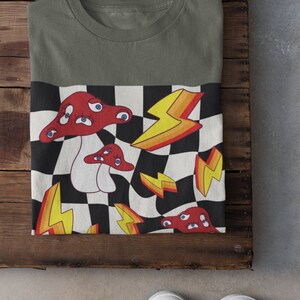 May include: A green t-shirt with a checkered pattern featuring red mushrooms with eyes and yellow lightning bolts.