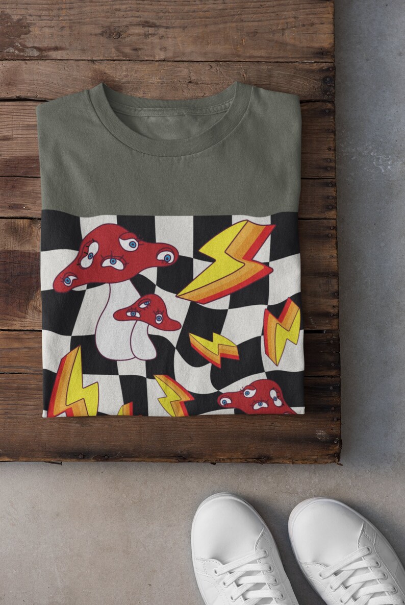 May include: A green t-shirt with a checkered pattern featuring red mushrooms with eyes and yellow lightning bolts.