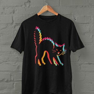 May include: A black short-sleeved t-shirt featuring a graphic of an arched-back cat. The cat design uses a layered, glitch-style effect with overlapping outlines in vibrant shades of pink, yellow, and cyan against the solid black fabric.