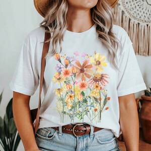 May include: White t-shirt with a colorful floral print featuring a variety of flowers in shades of yellow, orange, pink, and purple.