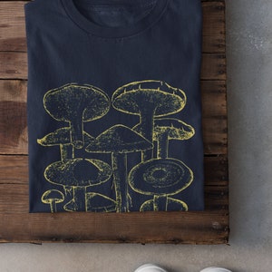 Pode incluir: Uma camiseta azul marinho com um gr&aacute;fico amarelo de um grupo de cogumelos.