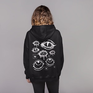 Peut inclure: Sweat-shirt à capuche noir avec un imprimé blanc de plusieurs yeux au dos.