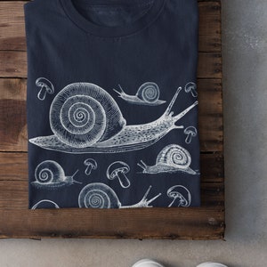 May include: A navy blue t-shirt with a white graphic print of snails and mushrooms.
