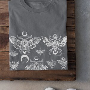 May include: A gray t-shirt with a white print of moths and crescent moons. The moths are stylized and have intricate details. The print is centered on the shirt and extends from the bottom hem to the middle of the shirt.