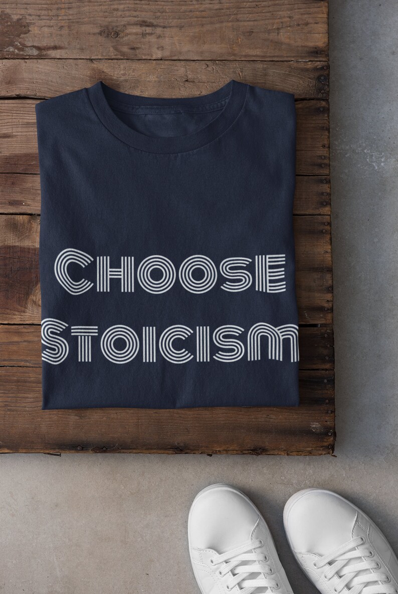 May include: A navy blue t-shirt with the text "CHOOSE STOICISM" printed in white. The text is in a retro, stylized font.