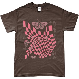 May include: A brown t-shirt with a pink checkered pattern, a butterfly, mushrooms, and stars. The checkered pattern is distorted, creating a wavy effect.