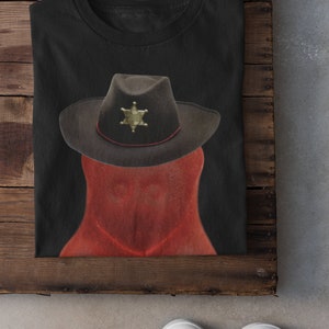 May include: A black t-shirt with a red and brown illustration of a sheriff's hat with a star badge.