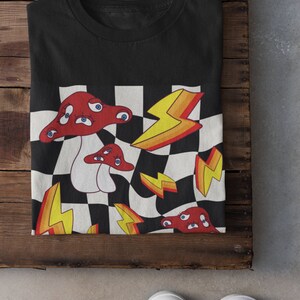 May include: Black t-shirt with a graphic print of red mushrooms with eyes on a checkered background with yellow lightning bolts.