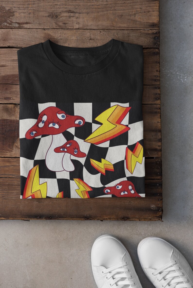 May include: Black t-shirt with a graphic print of red mushrooms with eyes on a checkered background with yellow lightning bolts.